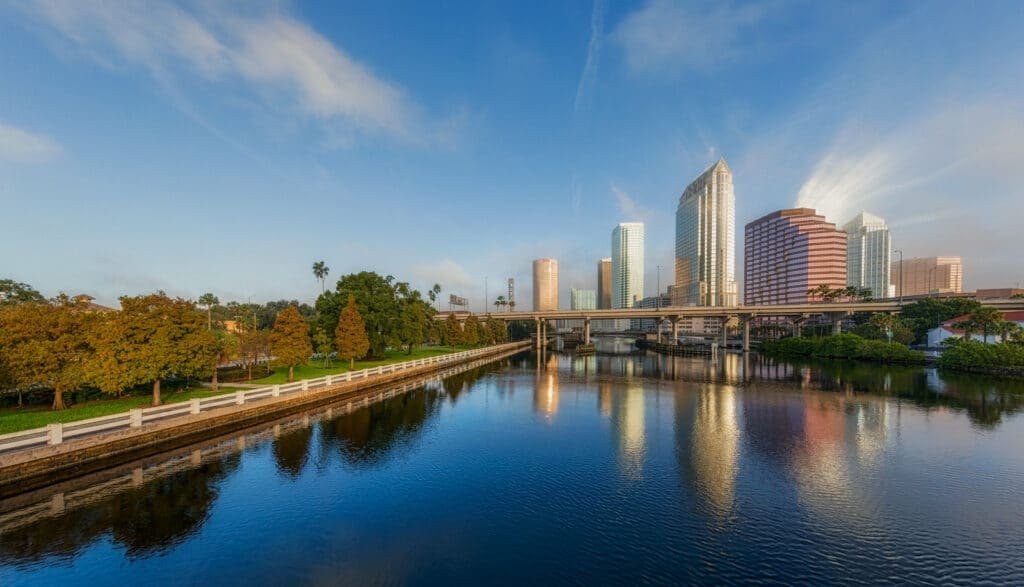 Um grande lago com prédios ao fundo e, na lateral esquerda, algumas árvores, para representar Tampa