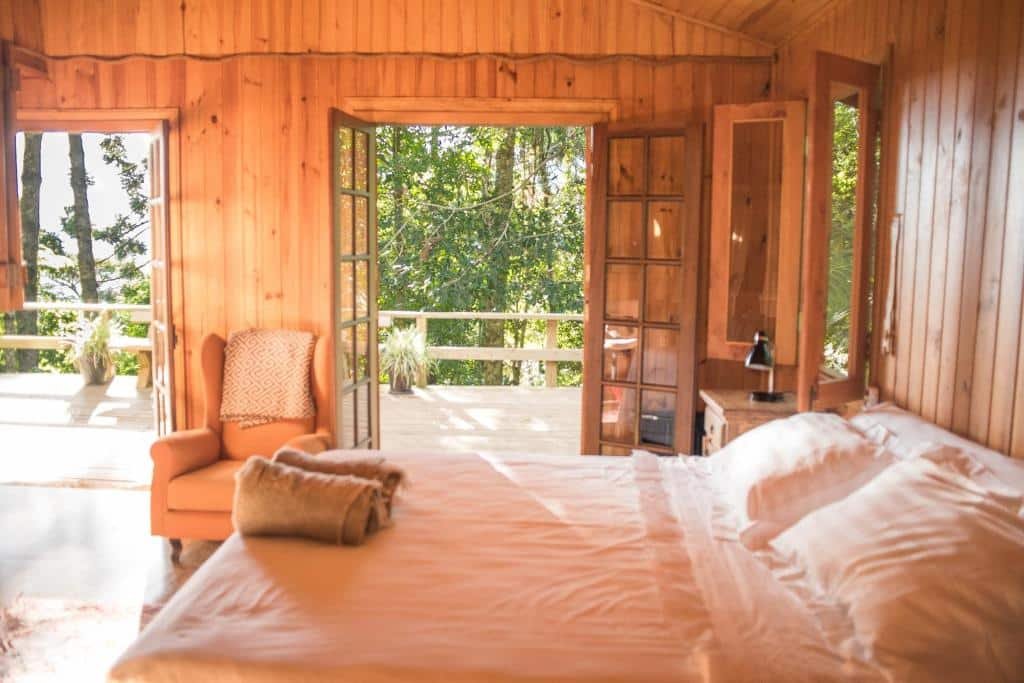Vista do quarto do Chalés Namaskar em São Bento do Sapucaí com cama ampla, poltrona, e  varanda.