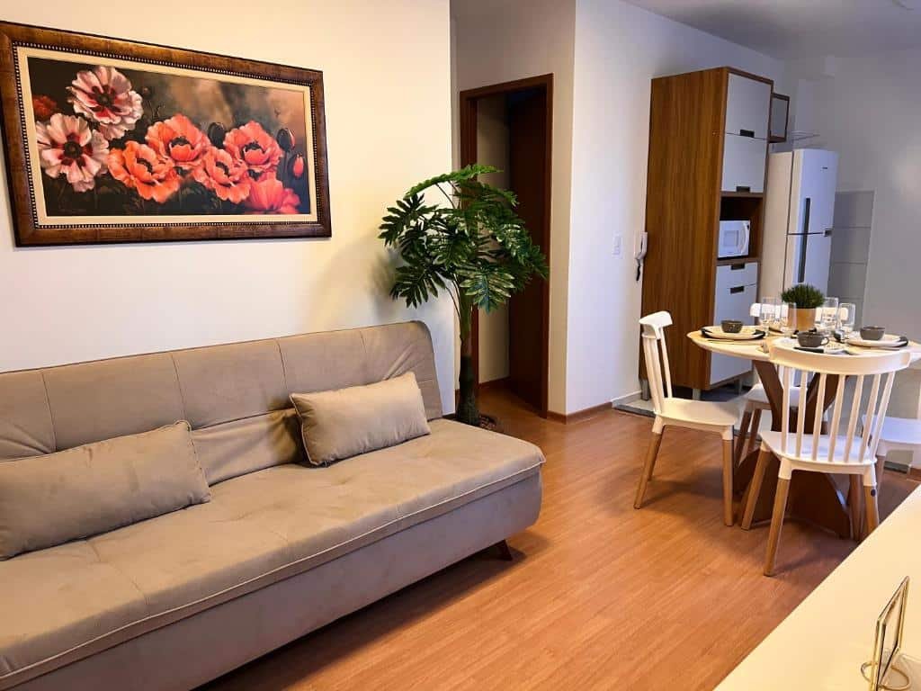 Sala de um apartamento com sofá no lado esquerdo, planta decorativa no lado direito do sofá, mesa redonda com quatro cadeiras e cozinha com armários e geladeira também a direita. Imagem para ilustrar o post hotéis em Caruaru.