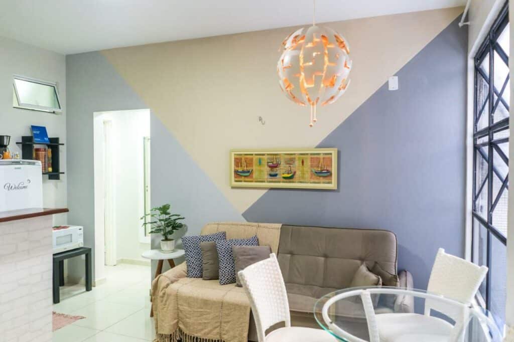 Sala de estar do Apartamento Beira Mar. Um sofá está no meio e perto de uma mesa redonda e algumas cadeiras. Ao lado é possível ver um pedaço da cozinha.