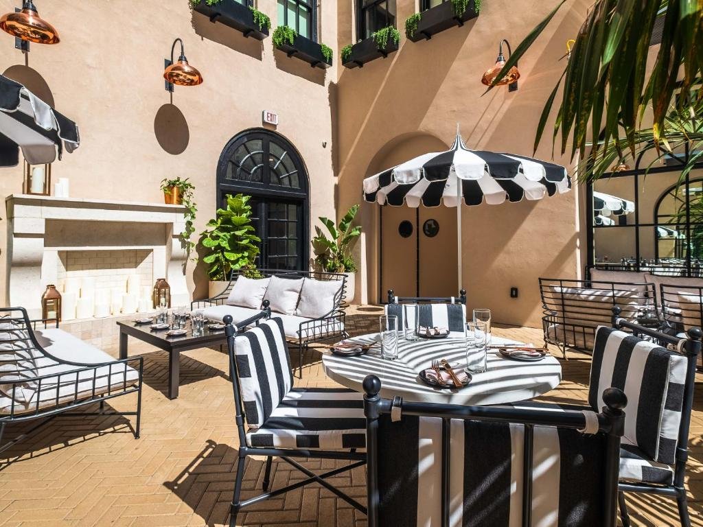 Vista da area de lazer do The Guild Hotel, San Diego, a Tribute Portfo com mesa e cadeiras com guarda-sol, sofá ao fundo com mesa de centro em um dia ensolarado. Representa hotéis em San Diego