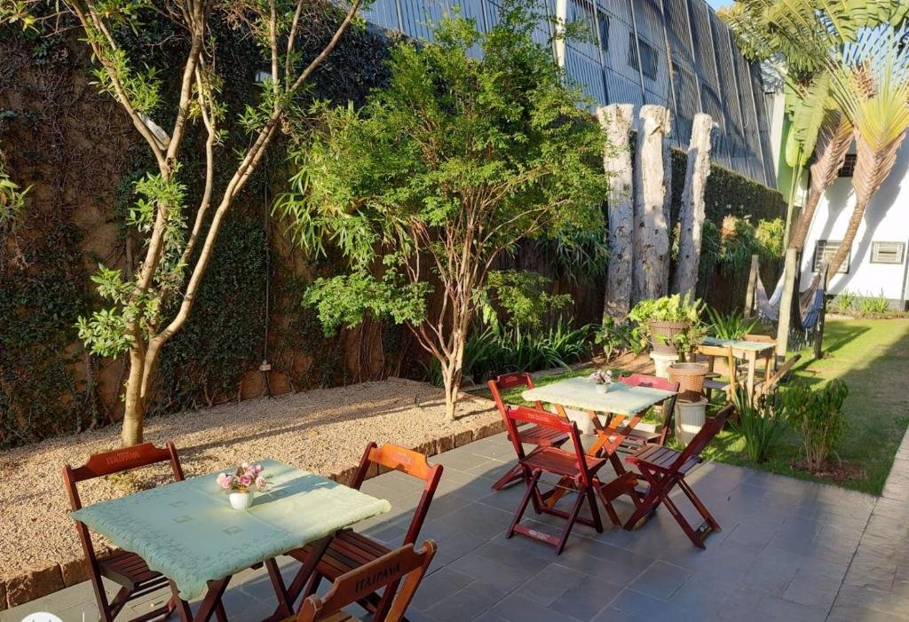 Vista da área de lazer do Shellter Hotel com duas mesas com quatro cadeiras de madeira no fundo do lado esquerdo redes de descanso. Representa hotéis em Holambra.