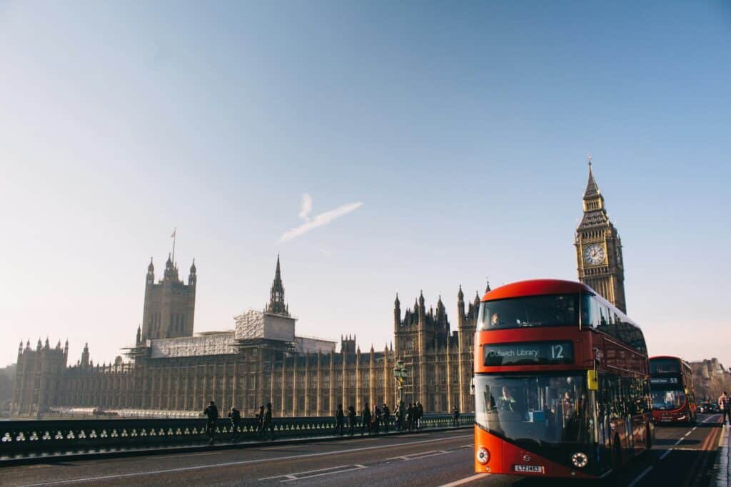 Ônibus vermelho de dois andares na Ponte de Westminster se aproxima do Parlamento e do Big Ben em um dia claro.