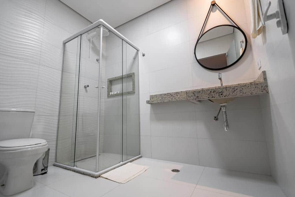 Banheiro privativo. Uma vaso sanitário no canto esquerdo, no meio o box de vidro e no canto direito a pia com um espelho. Foto para ilustrar post sobre Hotéis perto do Hospital Sírio Libanês.
