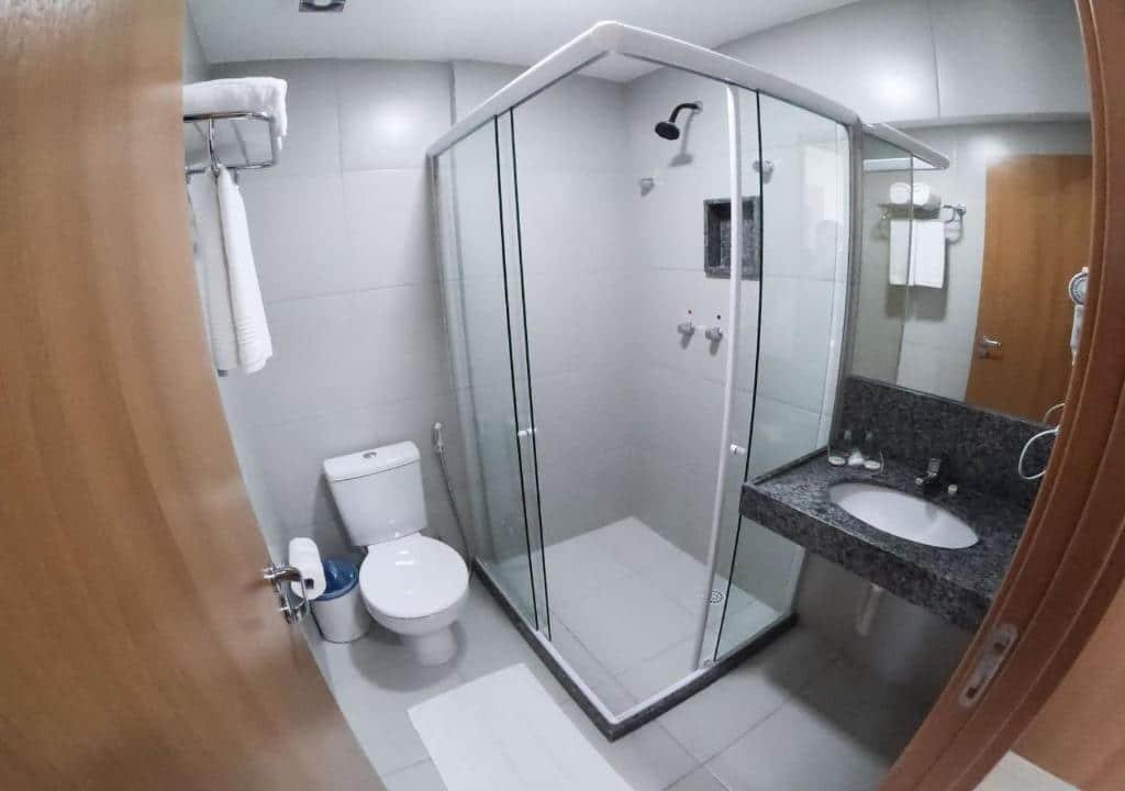Banheiro do quarto. Um box de vidro no meio, no lado esquerdo o vaso sanitário e toalhas. No lado direito a pia com um secador. Foto para ilustrar post sobre hotéis perto do Consulado Americano em Recife.