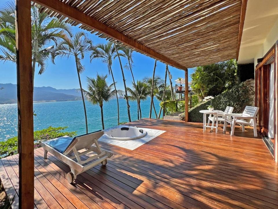 Deque do Barra do Piúva Porto Hotel com banheira de hidromassagem, espreguiçadeiras e mesinhas com cadeiras de frente para o mar.