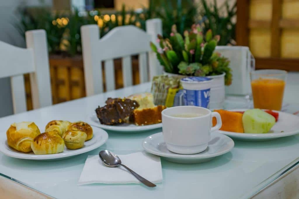 Uma mesa com café da manhã. Uma xícara, um prato com bolo, outro prato com salgados e outro com frutas; Um copo de iogurte. Foto para ilustrar post sobre Hotéis perto do Hospital Sírio Libanês.