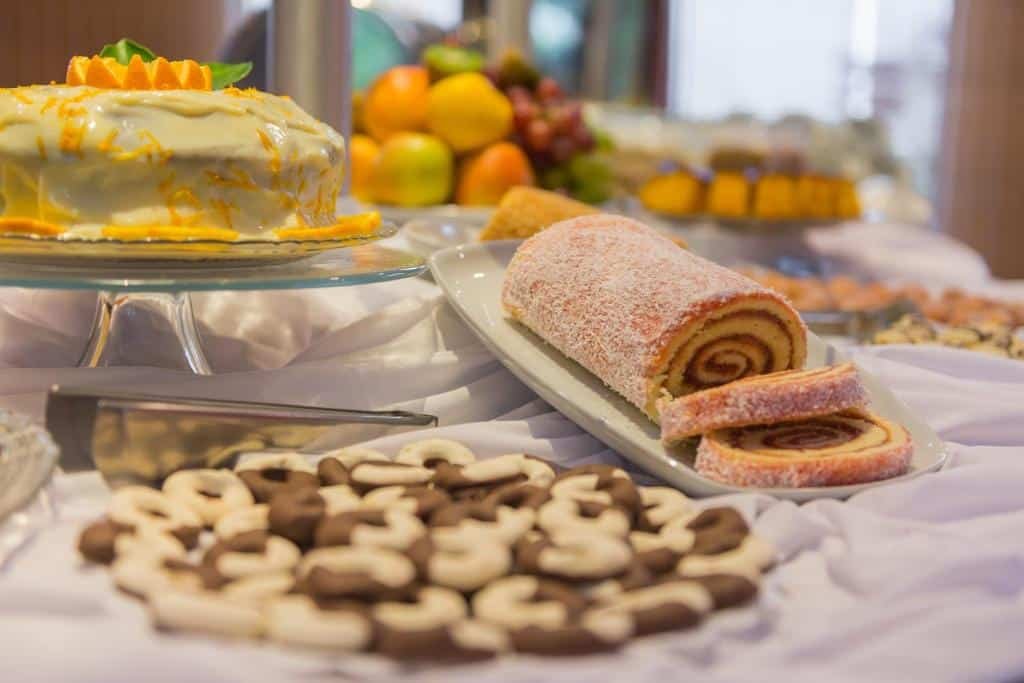 mesa de café da manhã do Hotel Plaza Norte Joinville com foco num rocambole doce de goiabada ao lado de um bolo confeitado de laranja.