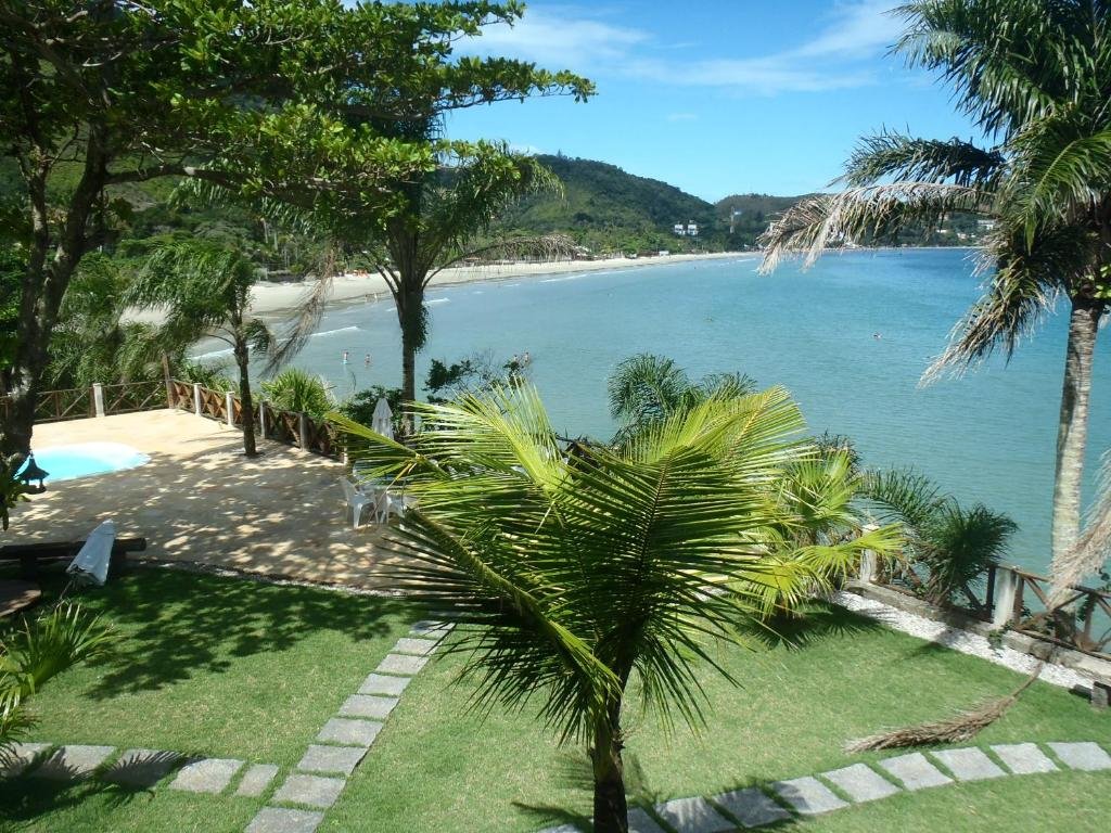 Área externa da Casa frente ao mar c/ piscina. Na frente um jardim com árvores, no canto direito a piscina, no fundo a vista do mar.
