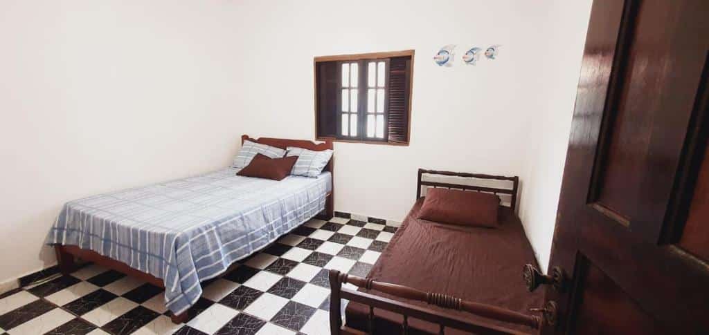 Quarto da Casa na Praia da Enseada. Do lado esquerdo uma cama de casal, do lado direito uma cama de solteiro. No meio uma janela.