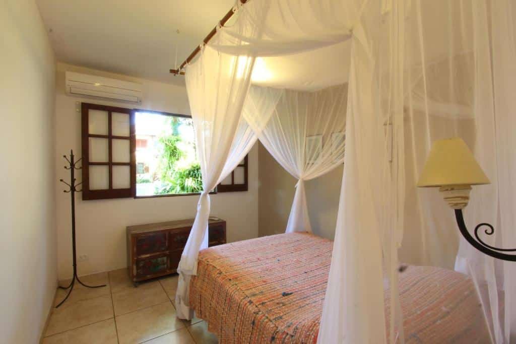 Quarto da Casa 32 Paraty. Uma cama de casal do lado direito com um abajur. De frente um cabideiro, uma cômoda, a janela do quarto e um ar-condicionado em cima.