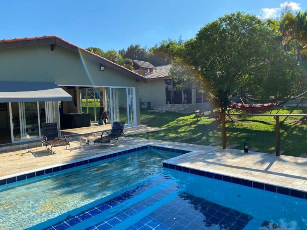 Piscina da Chácara Klein com um gramado ao redor, uma varanda com espreguiçadeiras e algumas redes de descanso por perto