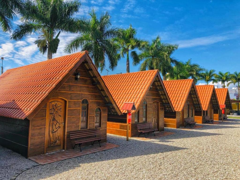 Parte do Chalé Caiçara em Caraguatatuba que mostra várias casinhas de madeira em formato de chalé uma do lado da outra com palmeiras atrás. Imagem ilustrando post Pousadas pet friendly no Litoral Norte de São Paulo.