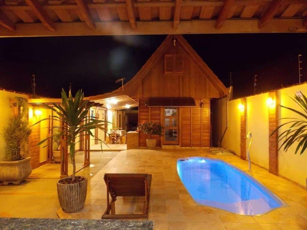 Parte externa do Chalé Paraíso com uma piscina no canto direito da imagem, ao fundo tem a construção do chalé em madeira e do lado esquerdo da piscina tem alguns vasos de planta e uma espreguiçadeira. Imagem ilustrando post Airbnb em Brotas.