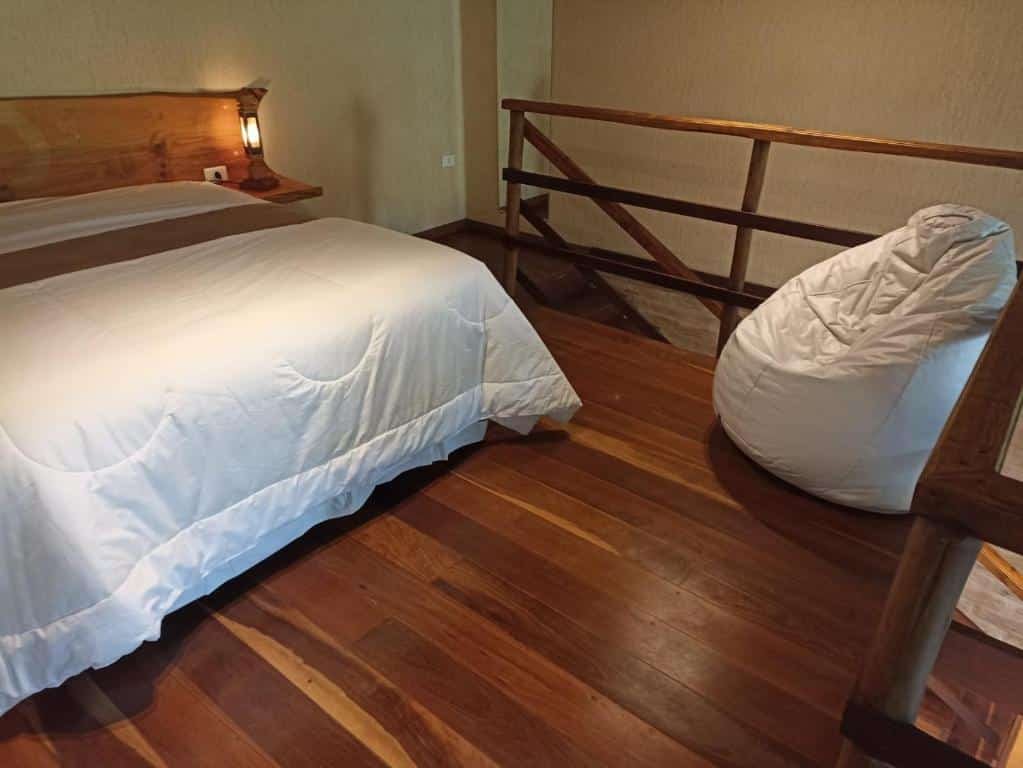 Quarto do Chalés Luar do Pico. Uma cama de casal do lado esquerdo, do lado direito um puff, atrás uma escada.