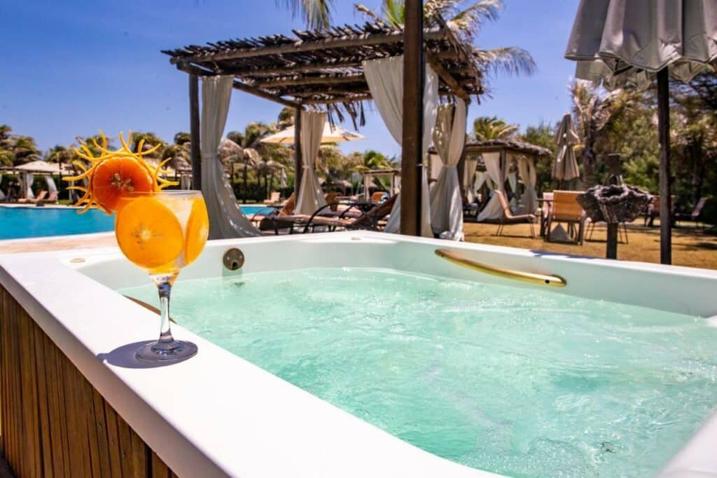 Hidromassagem do resort Dom Pedro Laguna. Ela está perto da piscina e de espaços de descanso com espreguiçadeiras. Uma bebida está em sua borda.
