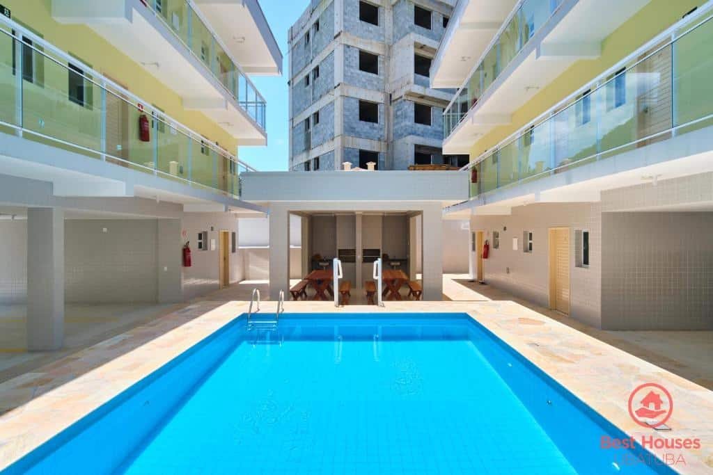 Área externa do Estúdios 3 Praias. De cada lado os prédios com varanda. No meio uma piscina e no fundo uma área gourmet.