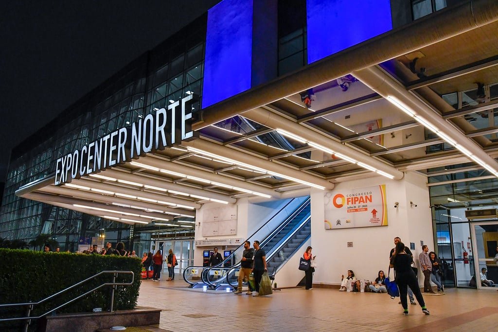Fachada do Expo Center Norte. Pessoas na frente, um prédio todo de vidro, no meio uma escada rolante.