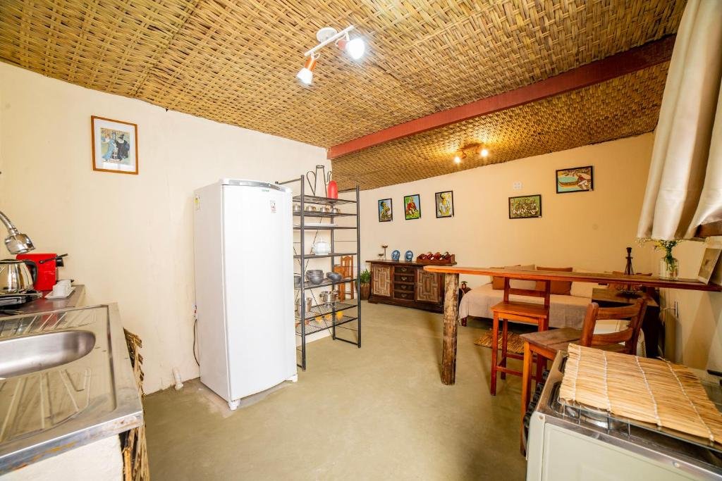 Cozinha do Ferraria Guest House. Do lado esquerdo a pia, a geladeira e as prateleiras. Do lado direito o fogão, uma bancada com duas cadeiras, no fundo um sofá cama e uma cômoda.