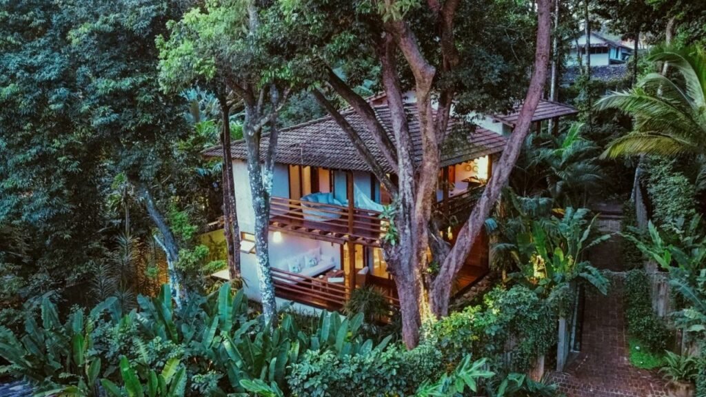 Vista da frente da Casa Hotel IFè Trancoso, próximo ao Quadrado durante o dia com a estadia no centro em volta de muitas árvores.