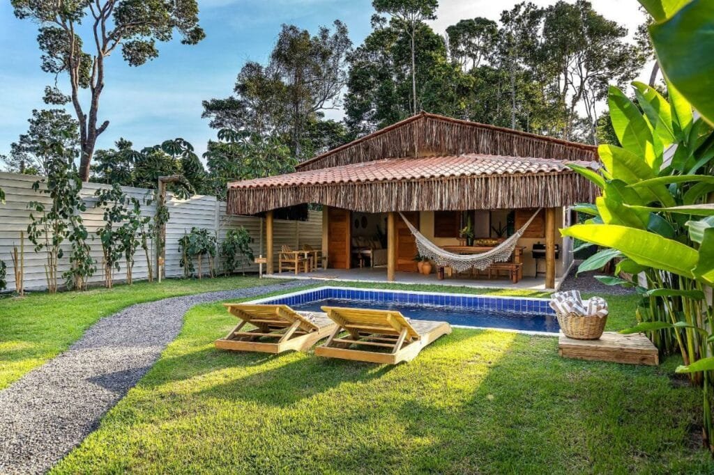 Frente da Casa Jenipapo Trancoso – Sinta o pedacinho do céu durante o dia com duas cadeiras a frente com vista para a piscina e ao fundo a casa.