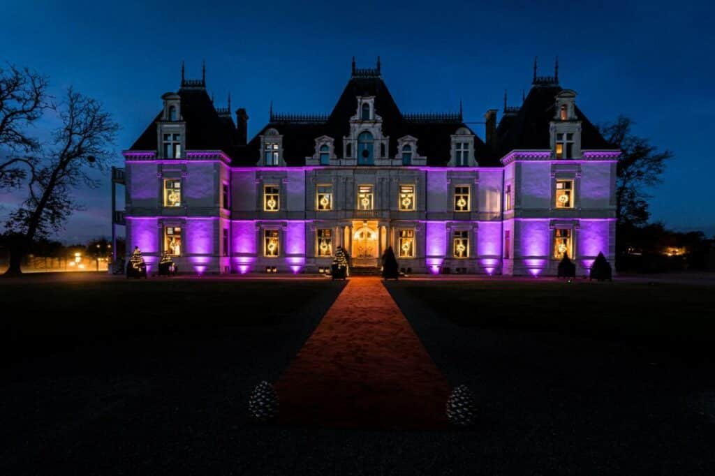 Frente do Château de Maubreuil durante a noite com jardim a frente e ao fundo o castelo iluminado.