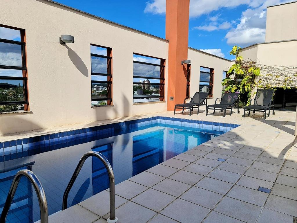 Piscina na cobertura do Hotel Germânia, em Joinville, no lado esquerdo da imagem, com três espreguiçadeiras ao fundo.