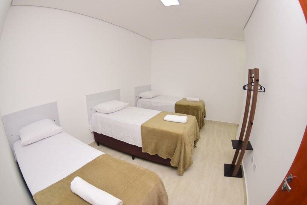 Quarto do Hotel Numaz Brás. Três camas de solteiro do lado esquerdo, do lado direito um cabideiro. Imagem para ilustrar post sobre hotéis perto do Expo Center Norte.