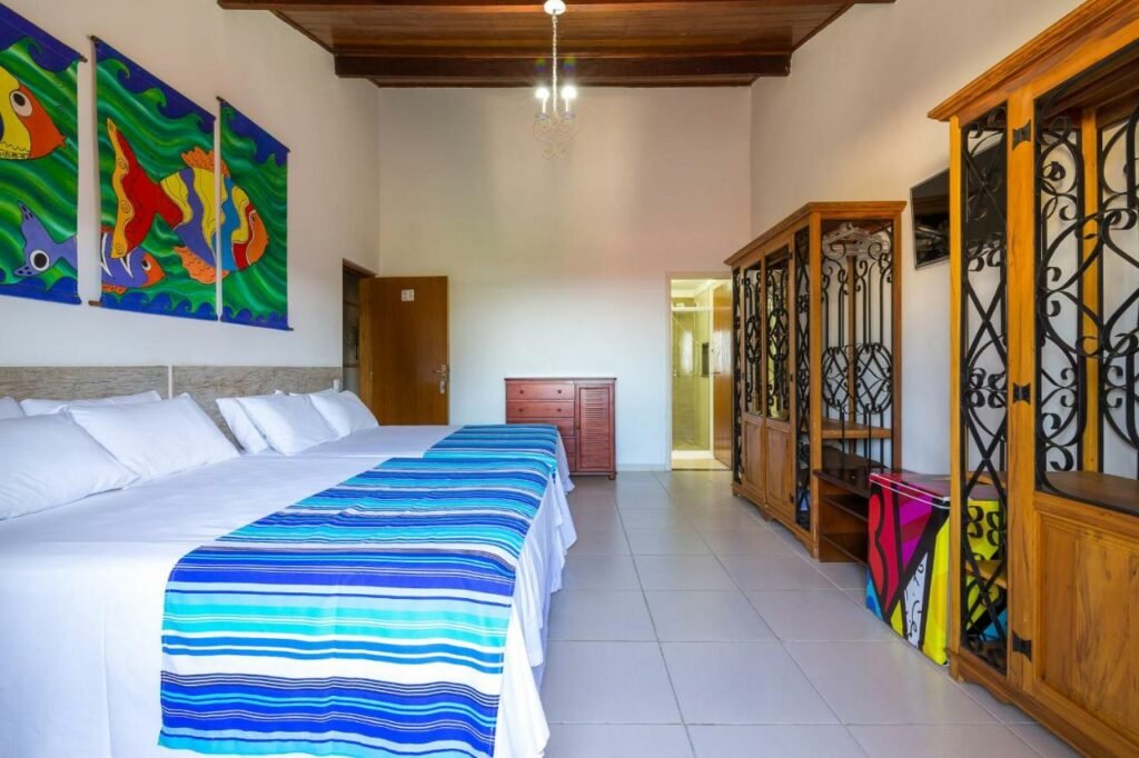 Quarto no Hotel Village Enseada com duas camas de casal, dois armários de conceito aberto, uma cômoda e um frigobar