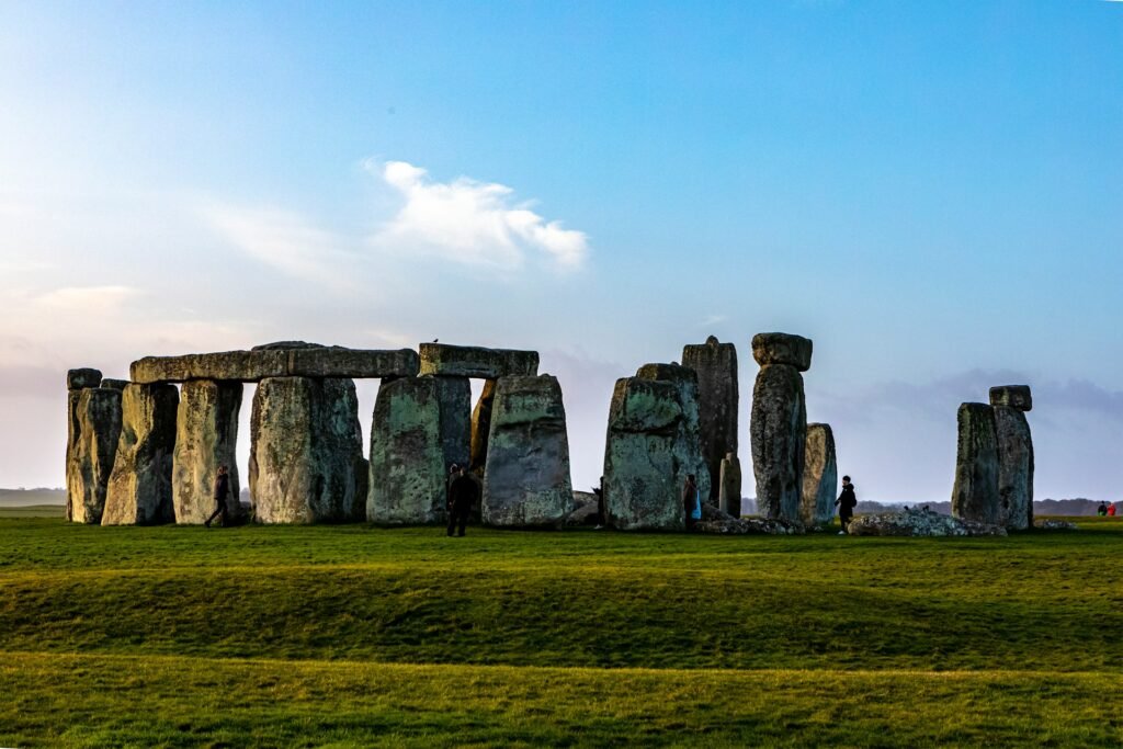 Vista ampla de Stonehenge com grandes pedras em pé em um campo gramado sob um céu azul com nuvens dispersas.