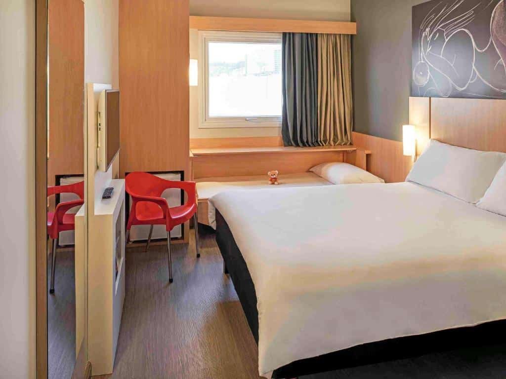 Quarto do ibis Jundiai Shopping com cama de casal, uma outra cama menor para criança, uma janela, um armário, uma televisão e um frigobar
