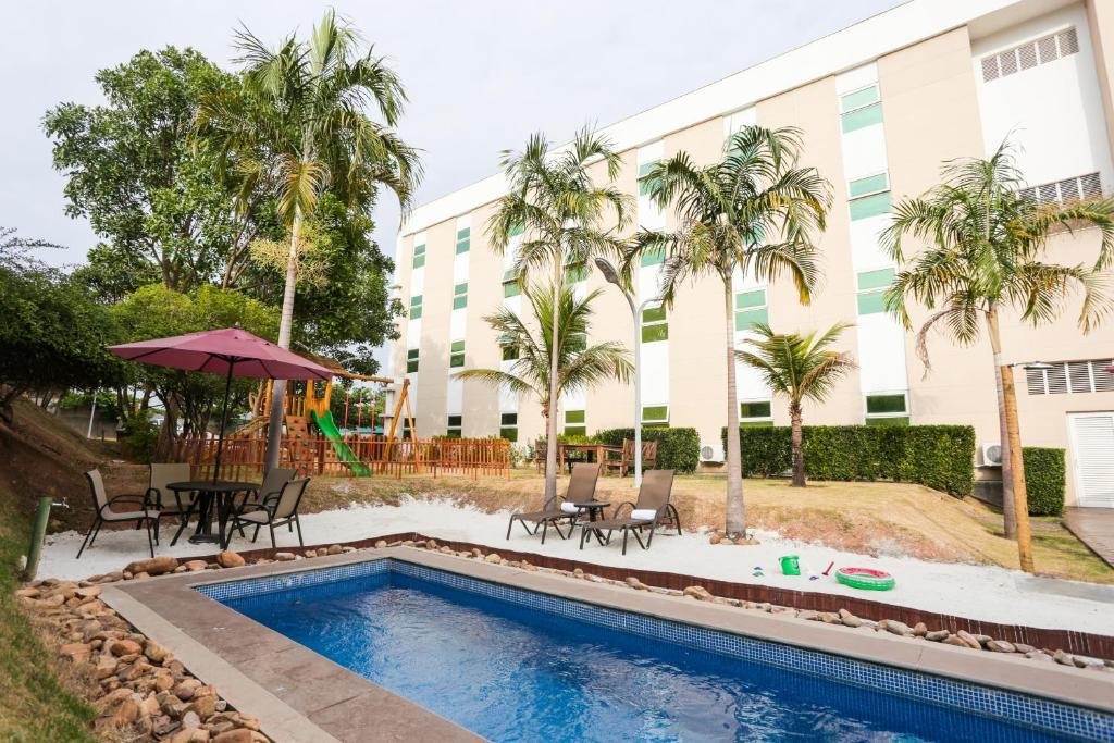 Piscina do Intercity Vinhedo com algumas árvores ao redor do deck e cadeiras, mesas e guarda-sóis, para representar hotéis perto do Hopi Hari