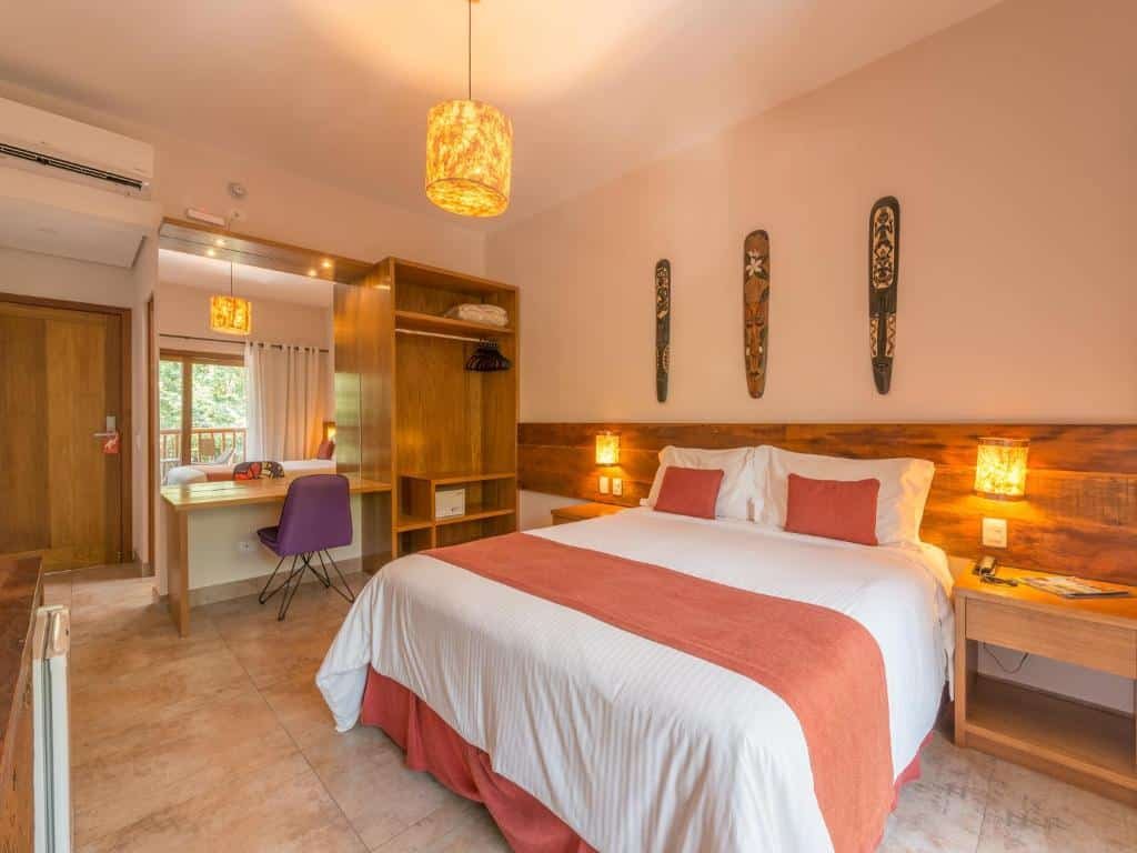 Quarto do Kalango Hotel Boutique com uma cama de casal, um armário de conceito aberto, uma mesa de escritório e uma cadeira, o chão é de piso frio, tudo decorado em madeira, para representar resorts em ilhabela