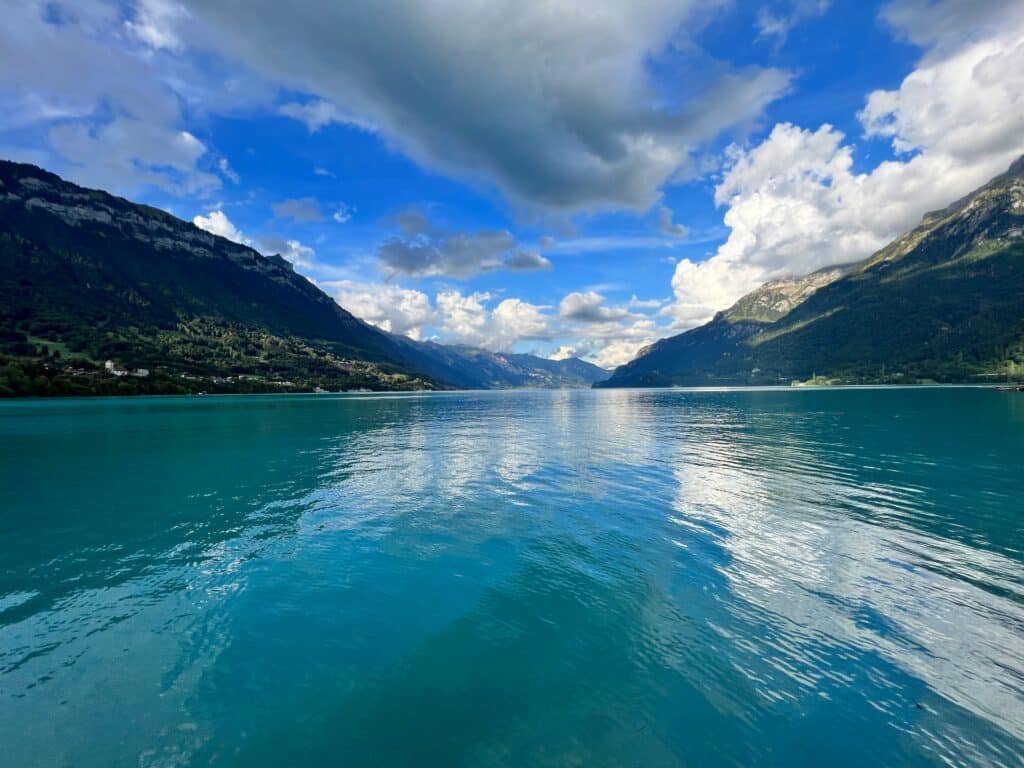 Lago Brienz com águas azul-turquesa é cercado por montanhas sob um céu azul com nuvens.