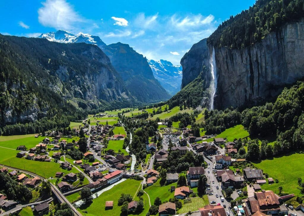Imagem da cidade de Lauterbrunnen, Suíça durante o dia com a cidade a frente em volta de arvores, montanhas e cachoeiras. Representa o que fazer na Suíça.