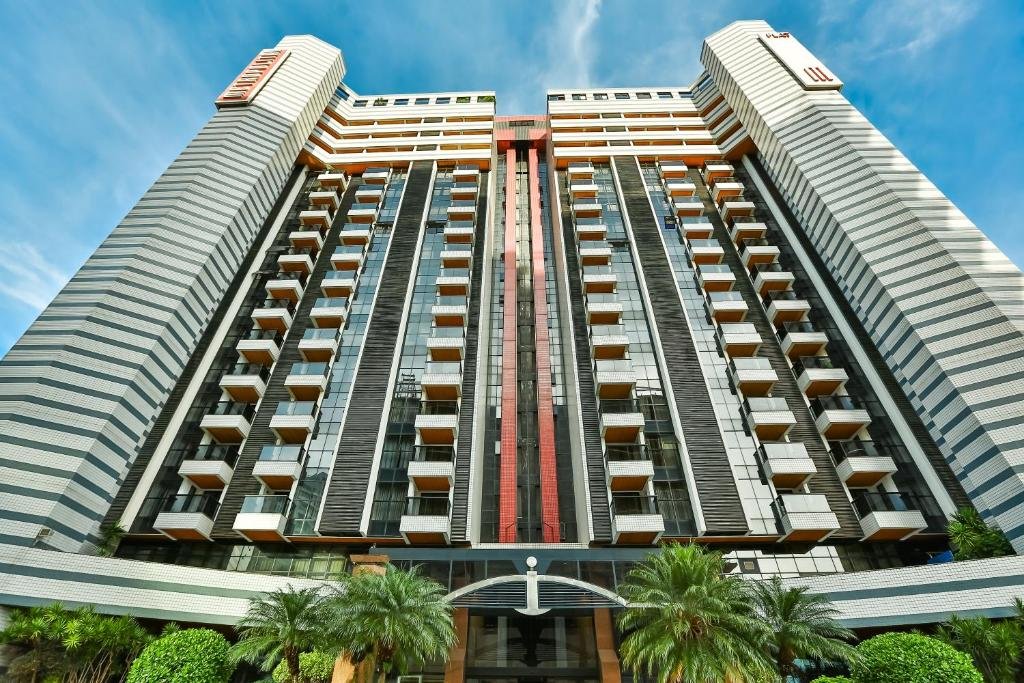 Prédio do Metropolitan Hotel Brasília com muitos andares, sacadas de vidro e o prédio em tons de cinza e vermelho