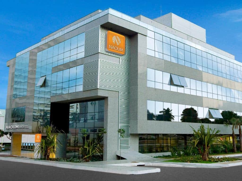 Prédio do Naoum Hotel com todas as janelas espelhadas e algumas árvores do jardim lateral da propriedade