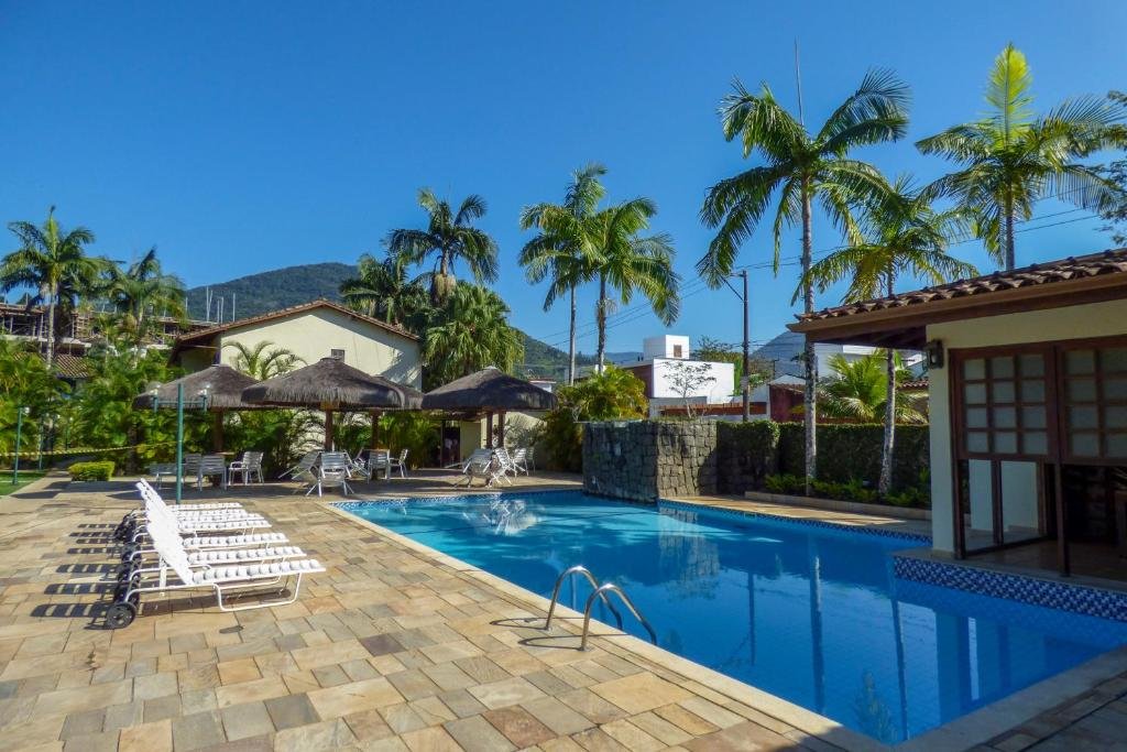 Área externa do Pedaço do Céu. Uma piscina grande, ao redor guarda-sóis, mesas, cadeiras e cadeiras de tomar sol.