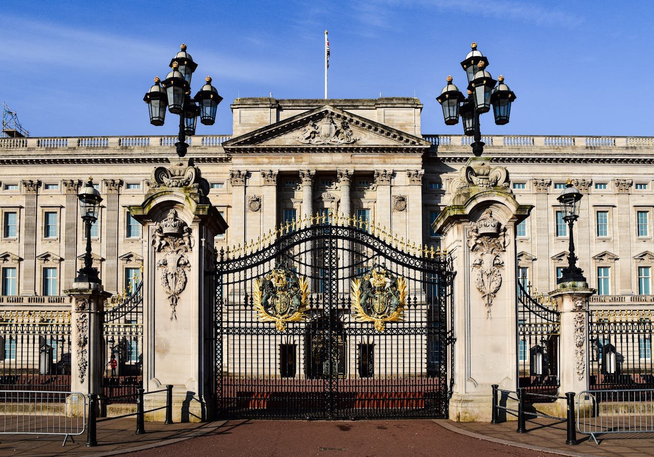 Vista frontal do Palácio de Buckingham com portões ornamentados e arquitetura clássica sob um céu azul claro. Essa é uma das atrações para incluir no roteiro para Londres.