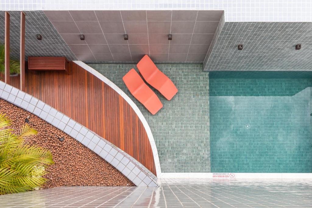 Área externa do Citi Hotel Residence Caruaru vista de cima. No lado esquerdo há um jardim e um banco de madeira e no lado direito uma pequena piscina com duas espreguiçadeiras colocadas na parte rasa. 