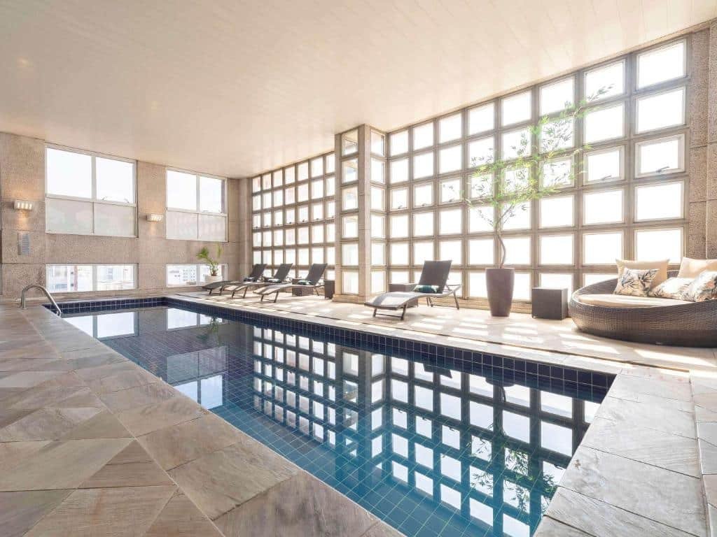 Piscina coberta, com cadeiras ao redor e bastante luz natural.
