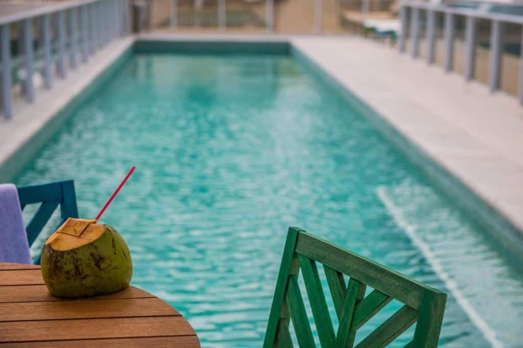 Uma mesa, com duas cadeiras e uma água de coco. Atrás um piscina. Foto para ilustrar post sobre hotéis perto do Consulado Americano em Recife.