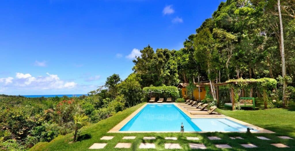 Vista da piscina da Vila Monjuá Trancoso durante o dia com piscina ao centro em volta arvores e mata.