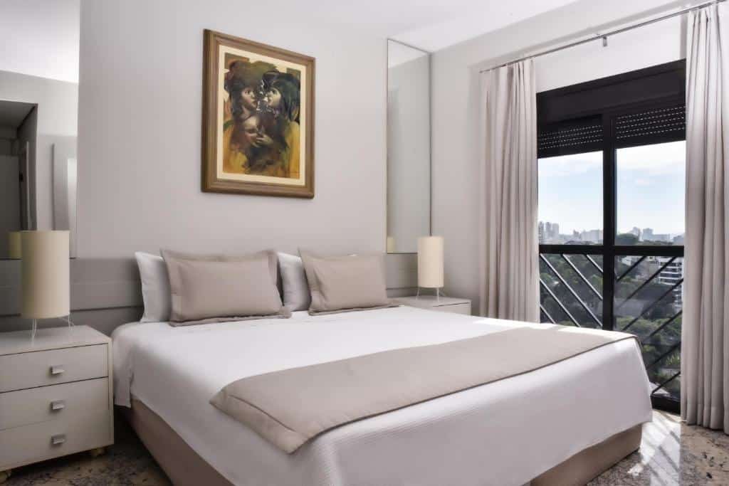 Quarto do Plaza Inn Small Town Flat. Uma cama de casal no centro, de cada lado uma cômoda, um abajur e um espelho. Do lado direito, uma parede de vidro com janela. Imagem para ilustrar post sobre hotéis perto do Expo Center Norte.