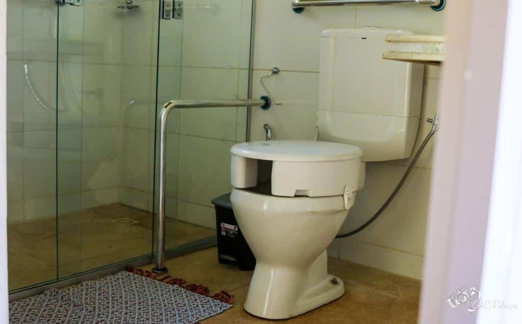 Imagem de um banheiro na Pousada e Restaurante Victórios, em Caeté. Está focando em uma privada adaptada para pessoas com mobilidade reduzida, e ao lado esquerdo dela há uma barra de apoio.