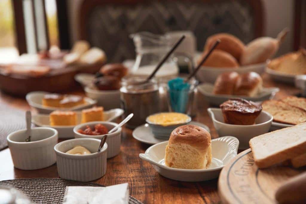 Foto da Pousada Pequena Tiradentes.  Nessa foto, podemos ver uma variedade de pães e condimentos dispostos sobre uma mesa. É um verdadeiro banquete visual que destaca os prazeres simples e deliciosos de um café da manhã ou brunch bem servido.