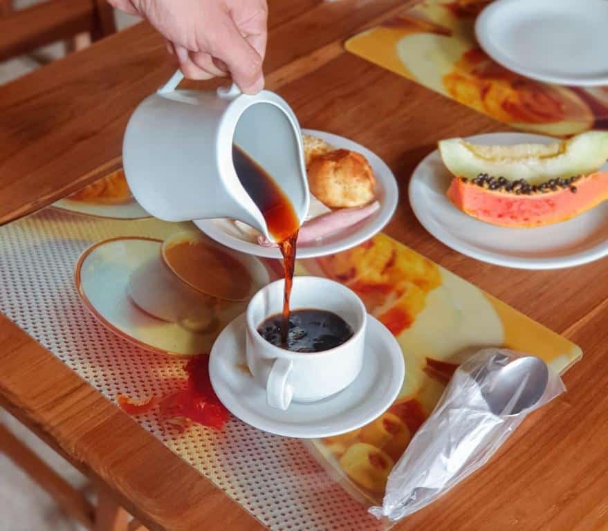 Foto da Pousada Quinta Do Conde, que capta um momento de café sendo servido de uma jarra branca em uma xícara. Há também um cenário de café da manhã que inclui frutas e pão, tornando-o uma cena convidativa de uma refeição matinal.