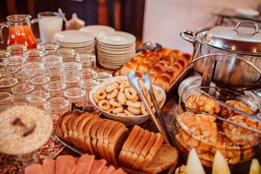 Foto da Pousada Montanhas do Sol.  A foto mostra uma variedade de alimentos dispostos em uma mesa, incluindo pães, bolachas, carnes frias e bebidas, preparados para um evento ou refeição especial. A abundância e a variedade tornam essa imagem visualmente atraente. 