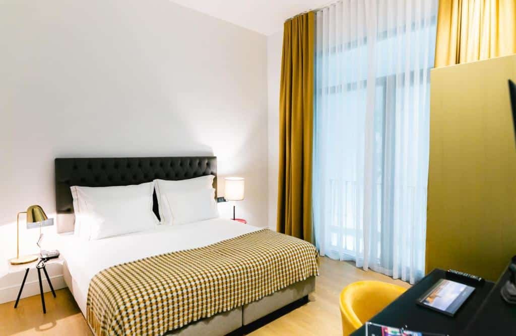 Quarto do Joya del Casco Boutique Hotel by Shiadu. Uma cama de casal com uma luminária de cada lado. De frente uma mesa de trabalho e uma televisão. No fundo a janela do quarto.