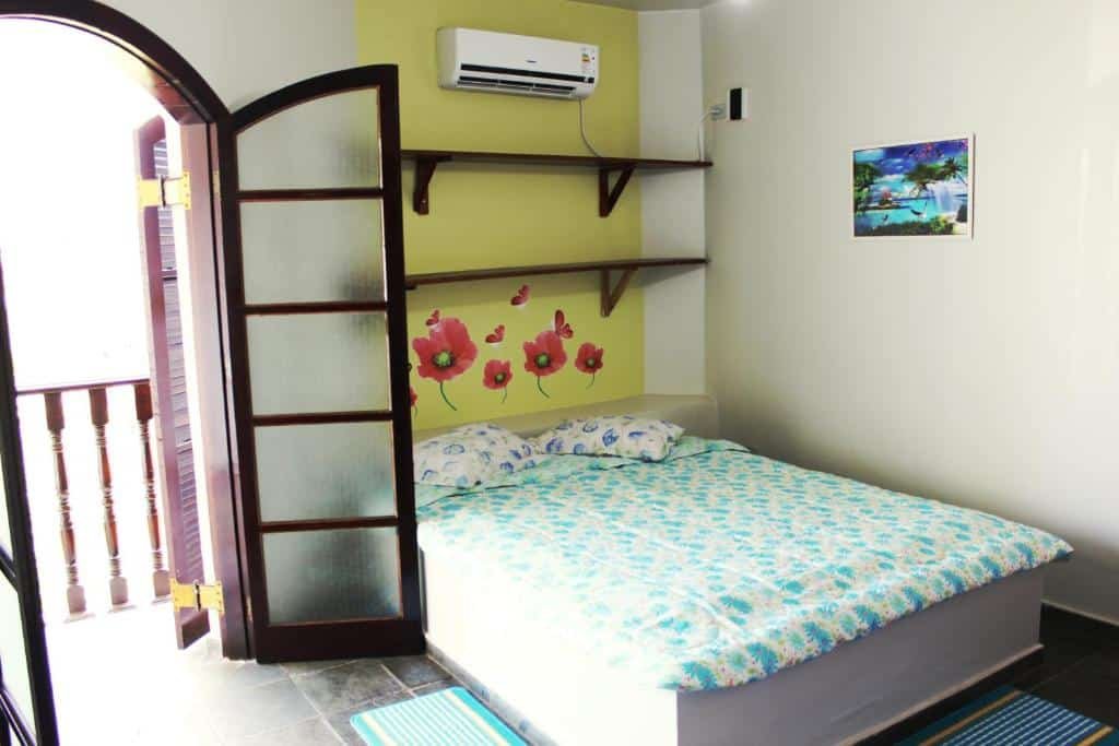 Quarto da pousada Farol das Gaivotas Pousada e Residence com uma cama de casal e na parede atrás da cama tem duas prateleiras e um ar-condicionado. Do lado da cama tem uma porta de vidro aberta que dá acesso a varanda do quarto.